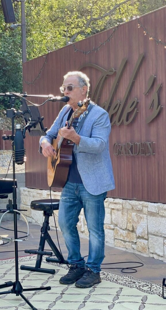 A man in sunglasses and a blue jacket playing guitar.